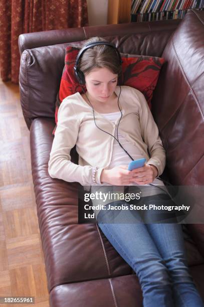 caucasian girl listening to headphones on sofa - lying on back girl on the sofa stock pictures, royalty-free photos & images