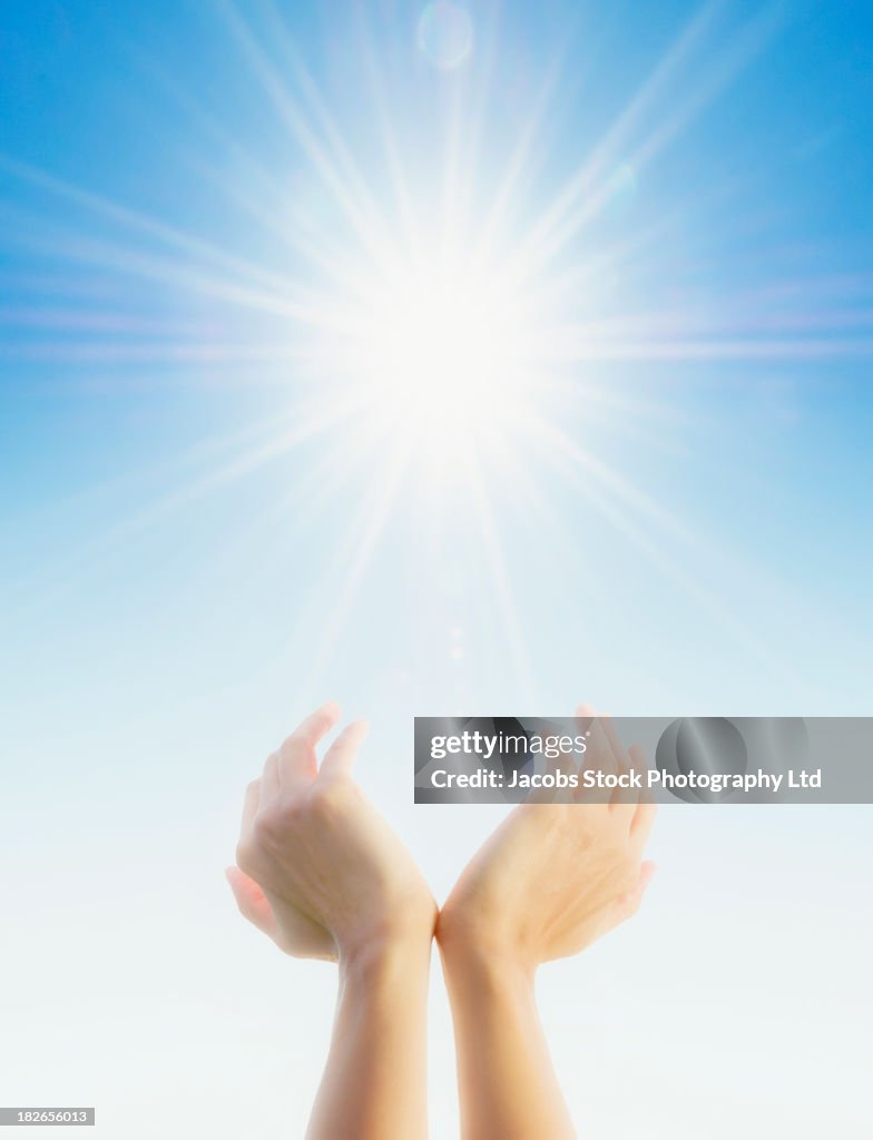 Hands cupping around sun in blue sky