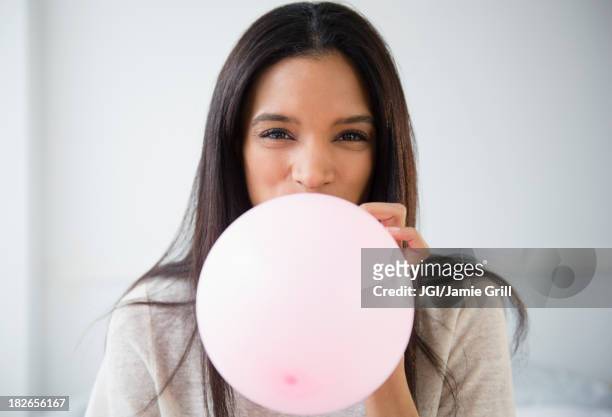 mixed race woman blowing up balloon - inflar fotografías e imágenes de stock