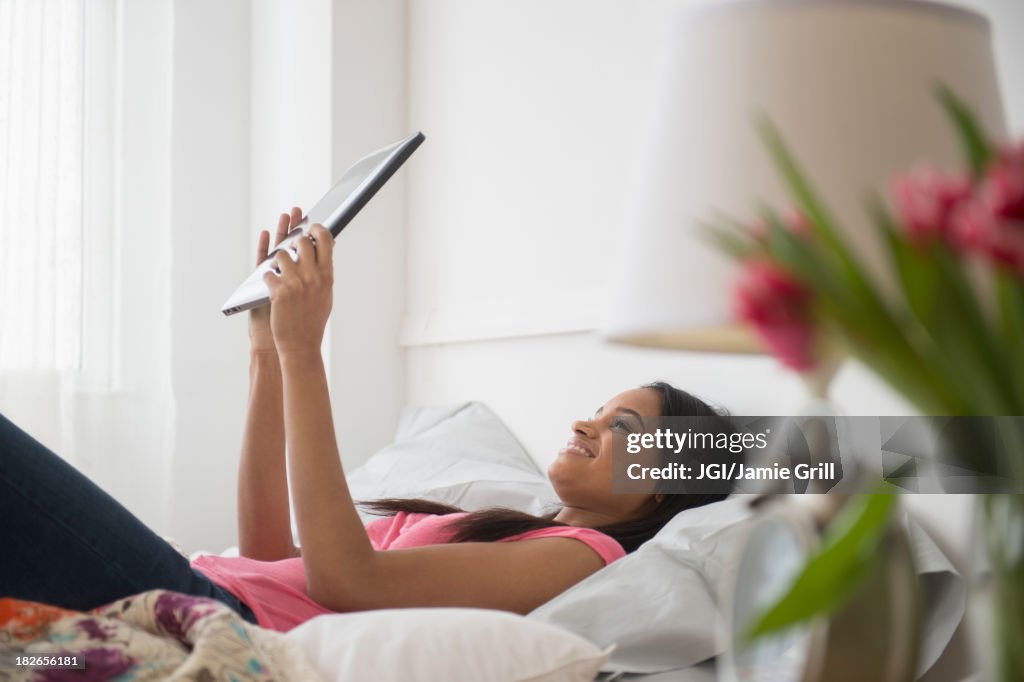 Mixed race woman using tablet computer on bed