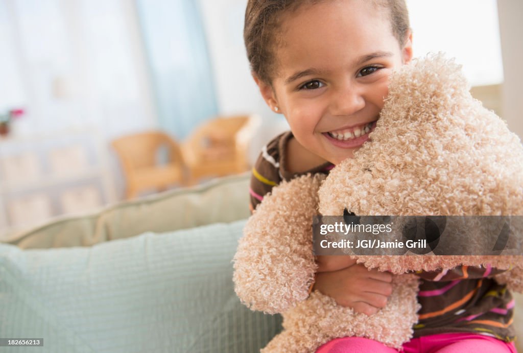 Hispanic girl hugging teddy bear on sofa