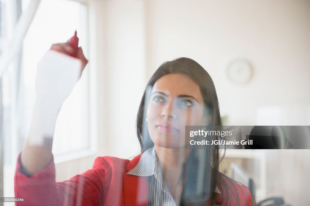 Indian businesswoman writing on glass in office