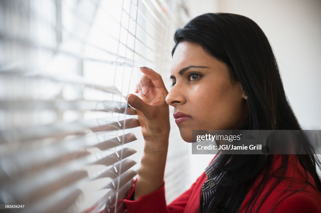 Indian businesswoman peering through blinds in office