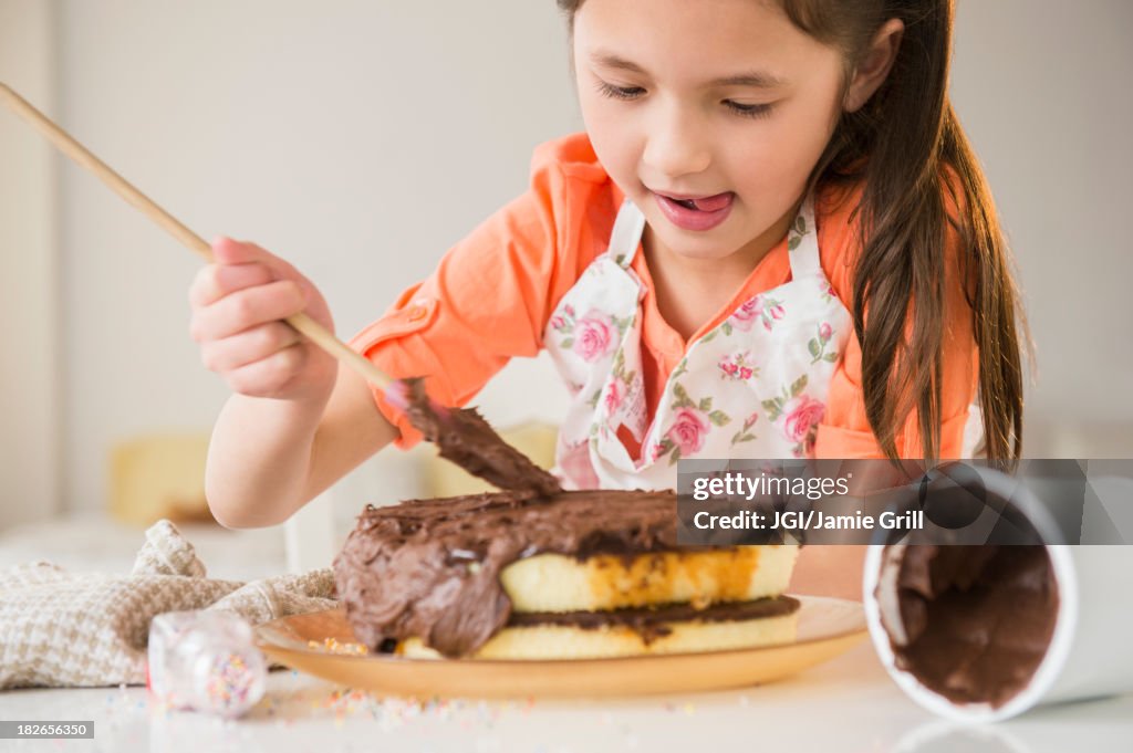 Mixed race girl icing cake in kitchen