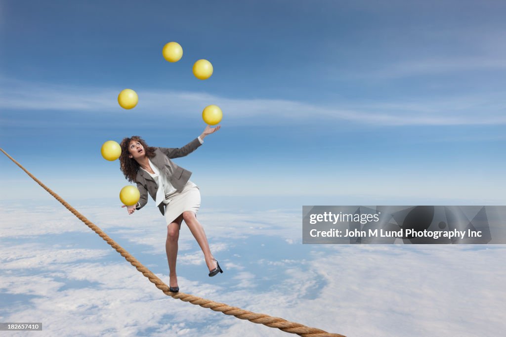 Mixed race businesswoman juggling on tightrope