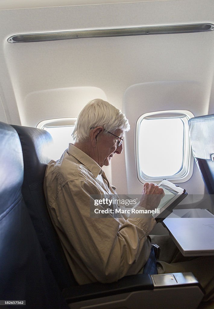 Older Caucasian man using tablet computer on airplane