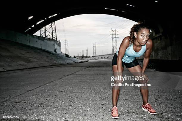 african american runner resting under overpass - läuferin stock-fotos und bilder
