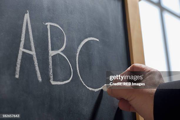 hispanic teacher writing 'abc' on chalkboard - rechtschreibung stock-fotos und bilder
