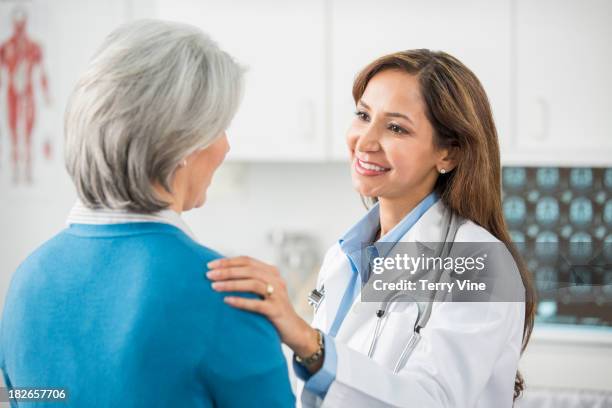 doctor talking with patient in office - man touching shoulder stock-fotos und bilder