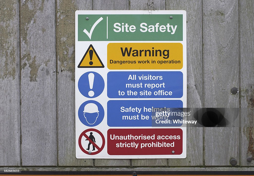 Construction site safety notices on wooden fence