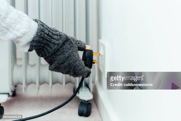 senior woman plugging in electric heater at home - fingerless glove stock pictures, royalty-free photos & images