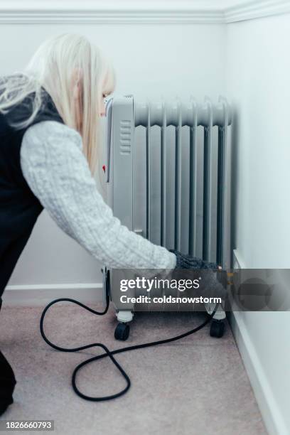 senior woman plugging in electric heater at home - fingerless glove stock pictures, royalty-free photos & images