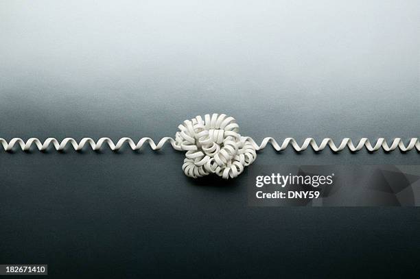 verschlungenes telefon kabel in einen knoten gebunden auf grauem hintergrund. - kommunikationsproblem stock-fotos und bilder