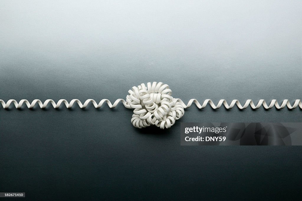 Coiled telephone cord tied in a knot on gray background