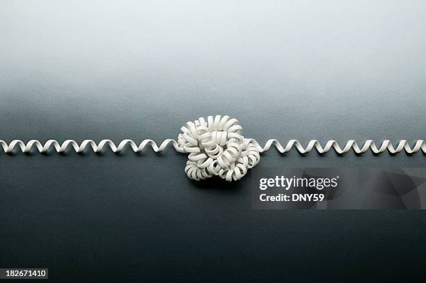 coiled telephone cord tied in a knot on gray background - flexes stock pictures, royalty-free photos & images