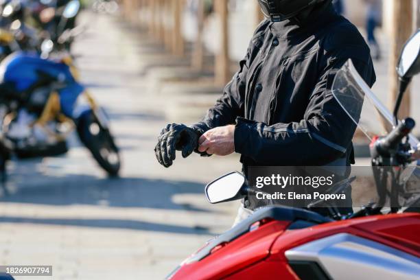man's hand putting on leather gloves against blurred motorbikes background - luva preta imagens e fotografias de stock
