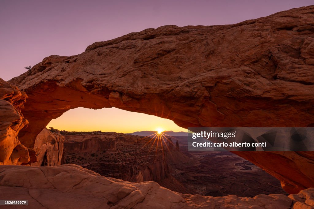 The sunlight envelope the Canyonlands valley during a summer sunrise, framed by Mesa Arch, Utah, United States of America