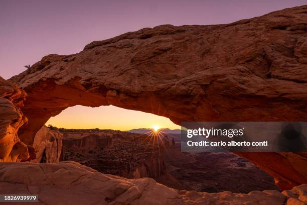 the sunlight envelope the canyonlands valley during a summer sunrise, framed by mesa arch, utah, united states of america - arches-national-park stockfoto's en -beelden