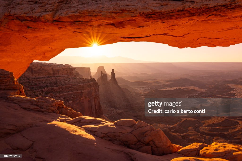 The sunlight envelope the Canyonlands valley during a summer sunrise, framed by Mesa Arch, Utah, United States of America