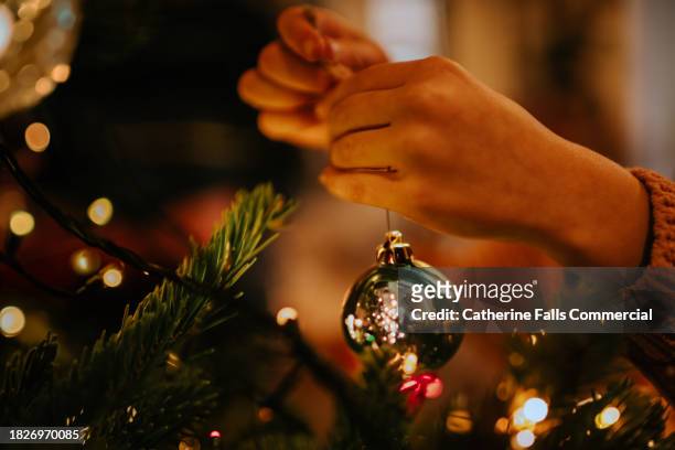 a child carefully places a shiny bauble on a christmas tree - pre positioned stock pictures, royalty-free photos & images