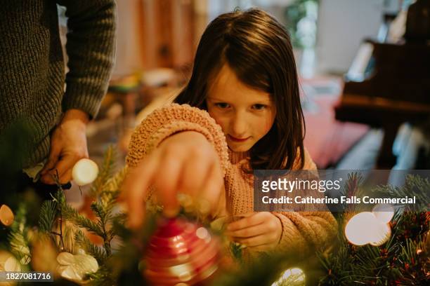 a little girl decorates a christmas tree - pre positioned stock pictures, royalty-free photos & images