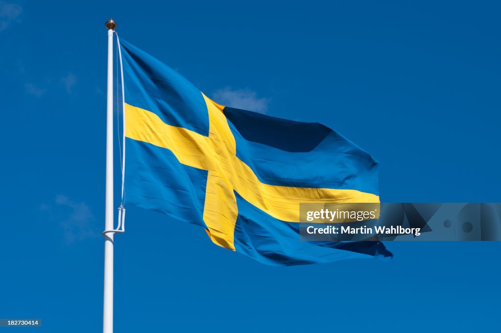 Flag of Sweden on flagpole rippling in wind against blue sky