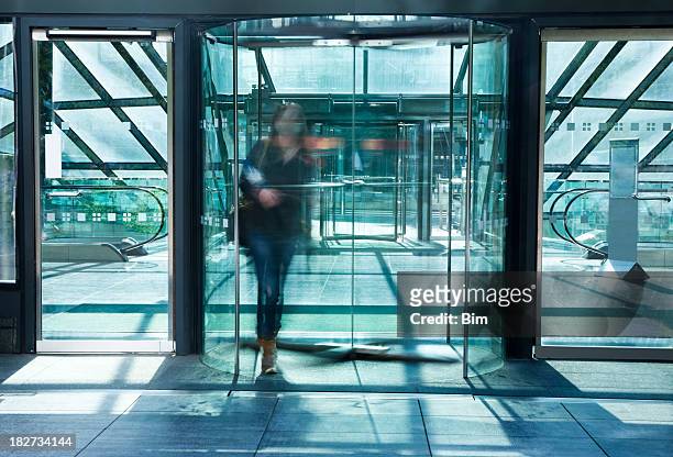 joven mujer caminando a través de una puerta giratoria de vidrio, borroso - revolve fotografías e imágenes de stock
