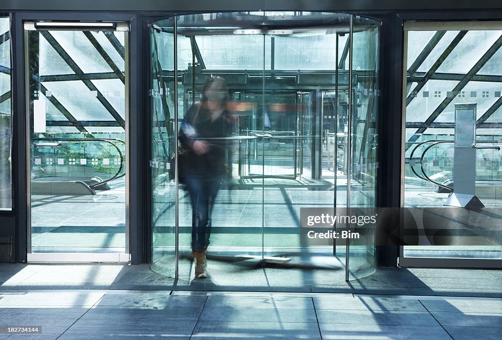 Giovane donna che cammina attraverso il vetro porta girevole, Immagine mossa