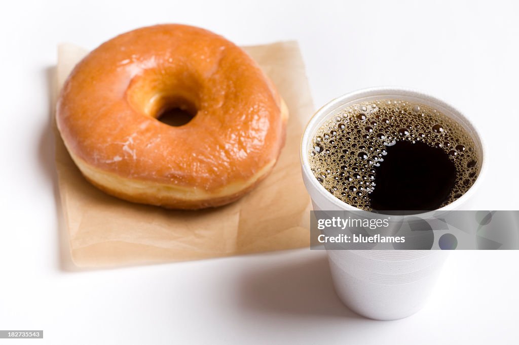 Close-up of a cup of black coffee and a glazed donut