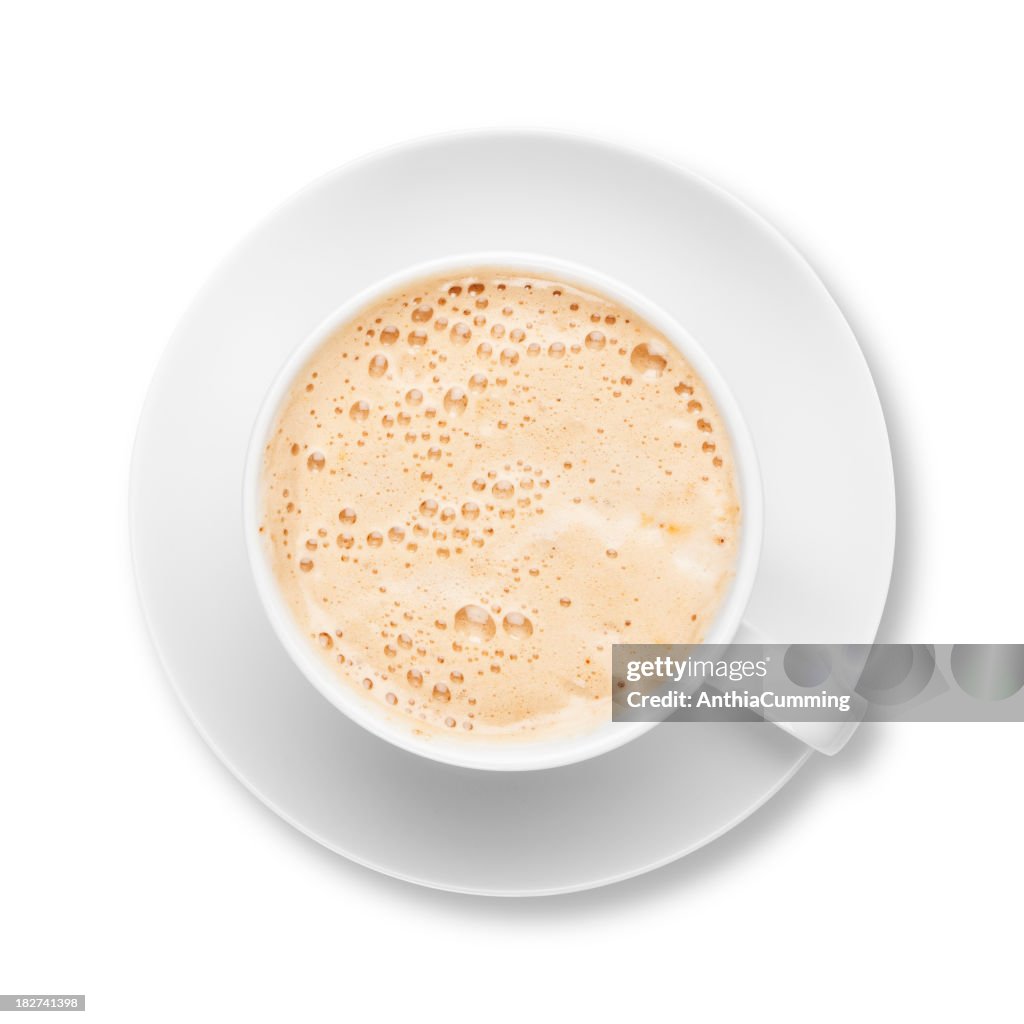 Fresh frothy latte coffee in white cup with saucer