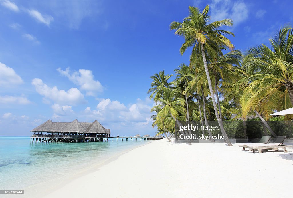 Spiaggia tropicale con sedie a sdraio e i bungalow sull'acqua