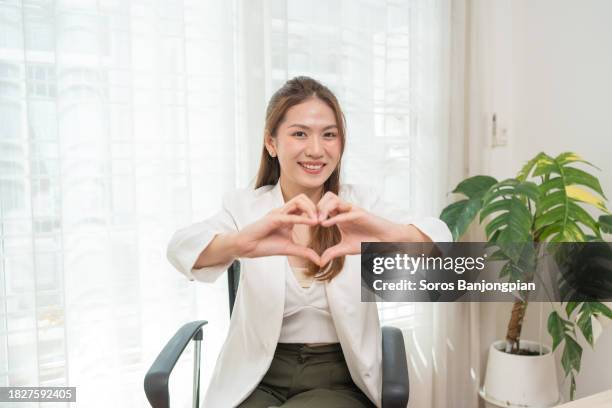 asian businesswoman beautiful and smart sitting in office. using hand make a heart shape. - truehearts stock pictures, royalty-free photos & images