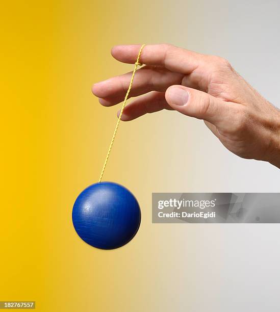 male hand playing with a blu yo-yo on yellow background - yo yo stock pictures, royalty-free photos & images