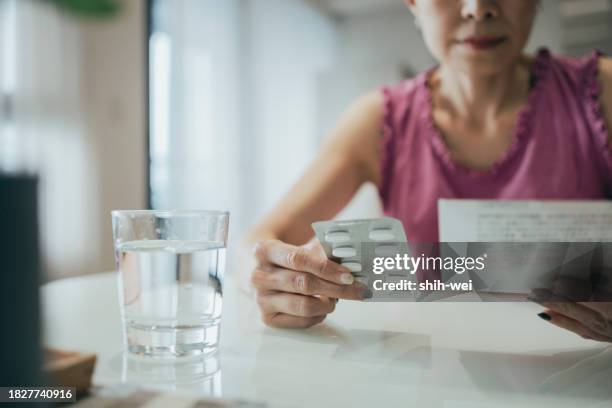 asian woman is carefully reviewing the patient information leaflet for her medication. - tomar remédio imagens e fotografias de stock