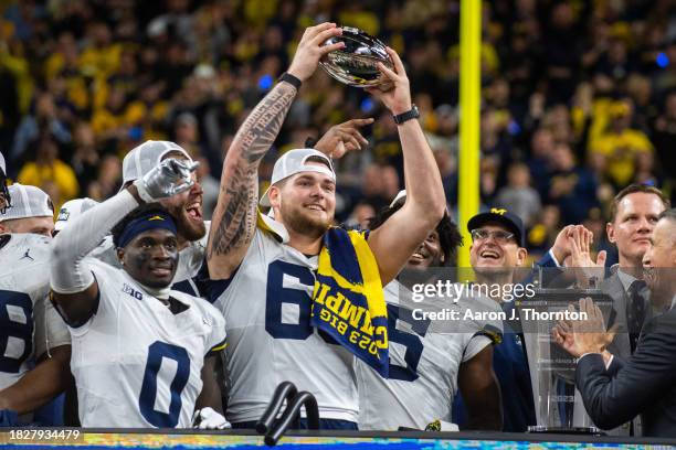 Mike Sainristil, Trevor Keegan, Zak Zinter, and Josaiah Stewart of the Michigan Wolverines celebrate with the Big Ten Championship trophy after...