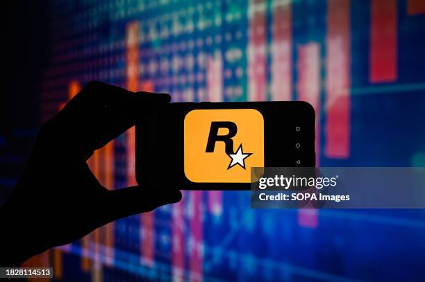 In this photo illustration a Rockstar Games logo is displayed on a smartphone with stock market percentages in the background.