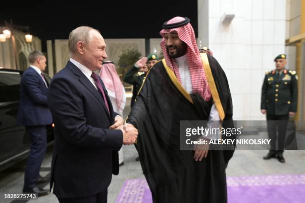 This pool photograph distributed by Russian state agency Sputnik shows Russia's President Vladimir Putin shaking hands with Saudi Crown Prince...