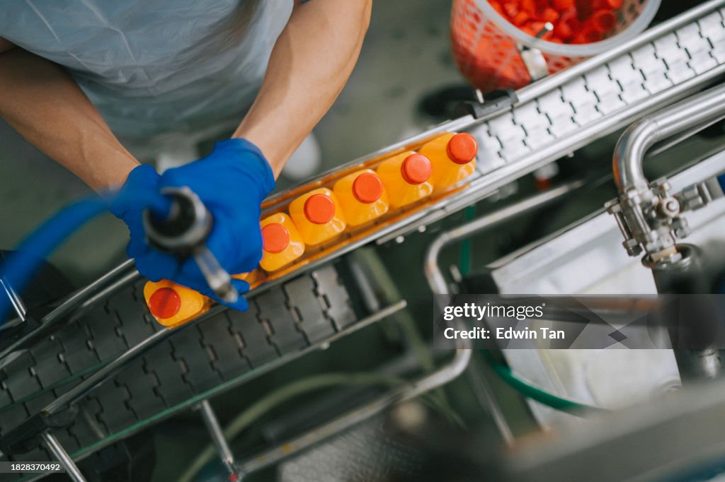 High angle view Asian Chinese juice factory worker sealing bottle cap of orange juice in production line