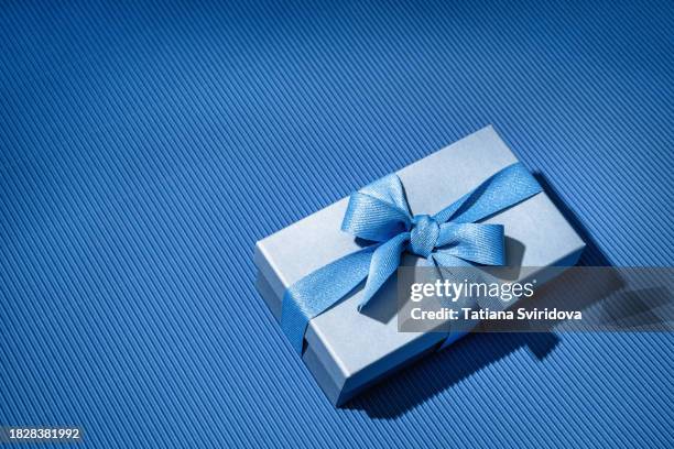 blue gift box with bow ribbon on blue gradient background - tienda-de-regalos fotografías e imágenes de stock
