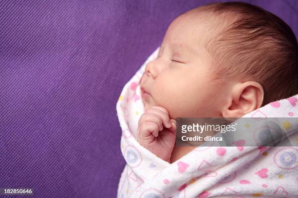 a newborn girl sleeping while being swaddled - purple hat stockfoto's en -beelden