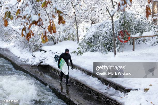 Surfer walks along the side of the Eisbach on December 3, 2023 in Munich, Germany. The Eisbach, wave is a man-made wave in the river that the flows...