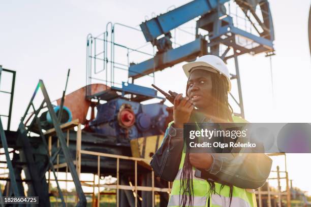 female engineer with walkie-talkie working on oil drilling field in sunny day - raffinerie photos et images de collection