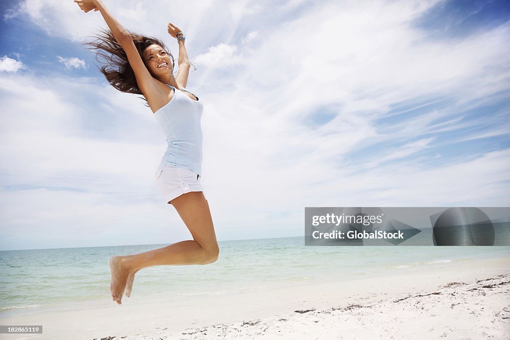 Excited woman jumping with hands raised on beach