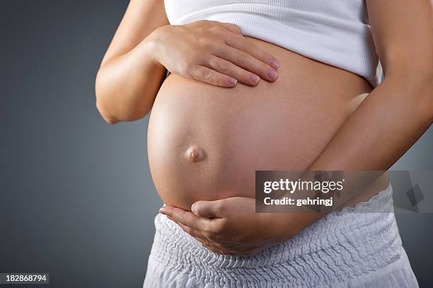 a pregnant woman feels for her baby kicking with both hands - belly button stock pictures, royalty-free photos & images