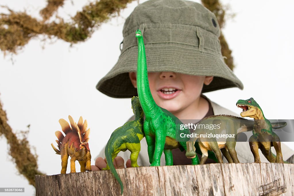 Young boy wearing safari outfit playing with toy dinosaurs 
