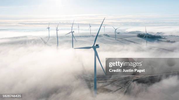 a drone/aerial view of a wind farm of wind turbines sitting proud above the low lying mist on a winter's morning - cloudscape stock pictures, royalty-free photos & images