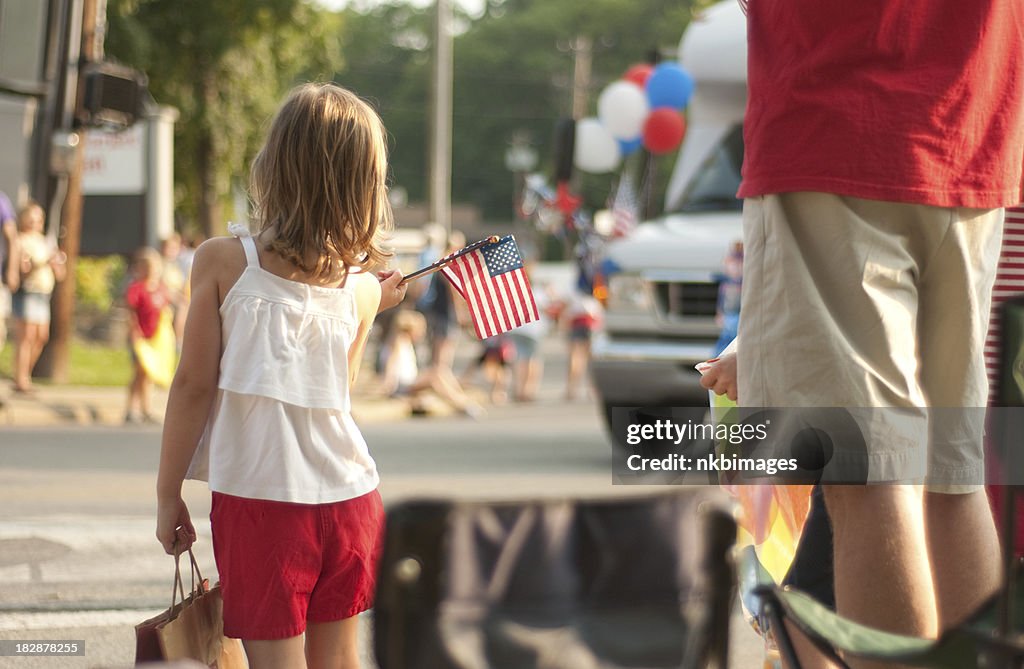 Girl with flags watches 4th of July parade in America