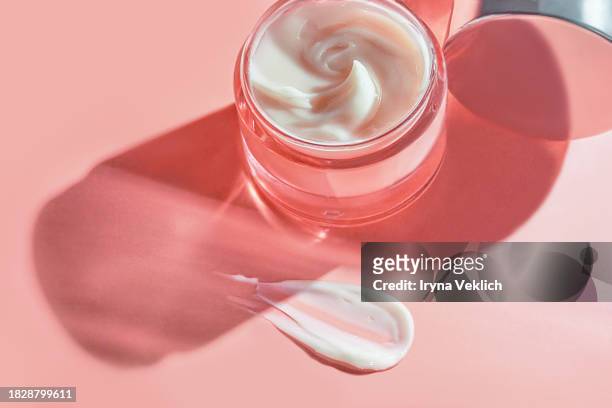 texture of cosmetic product in glass jar  - skincare face cream, refreshing hydration water cream or hand cream on natural pastel pink colour background. - hair treatment stock-fotos und bilder