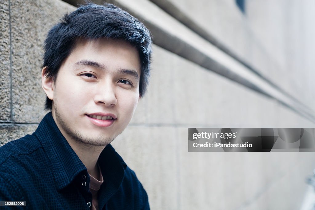 Portrait of young Asian man smiling with wall as background