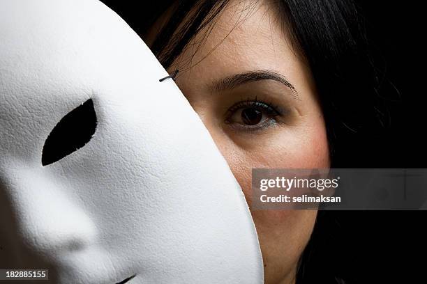 woman with black hair and eyes peeking behind white mask - mask disguise stockfoto's en -beelden